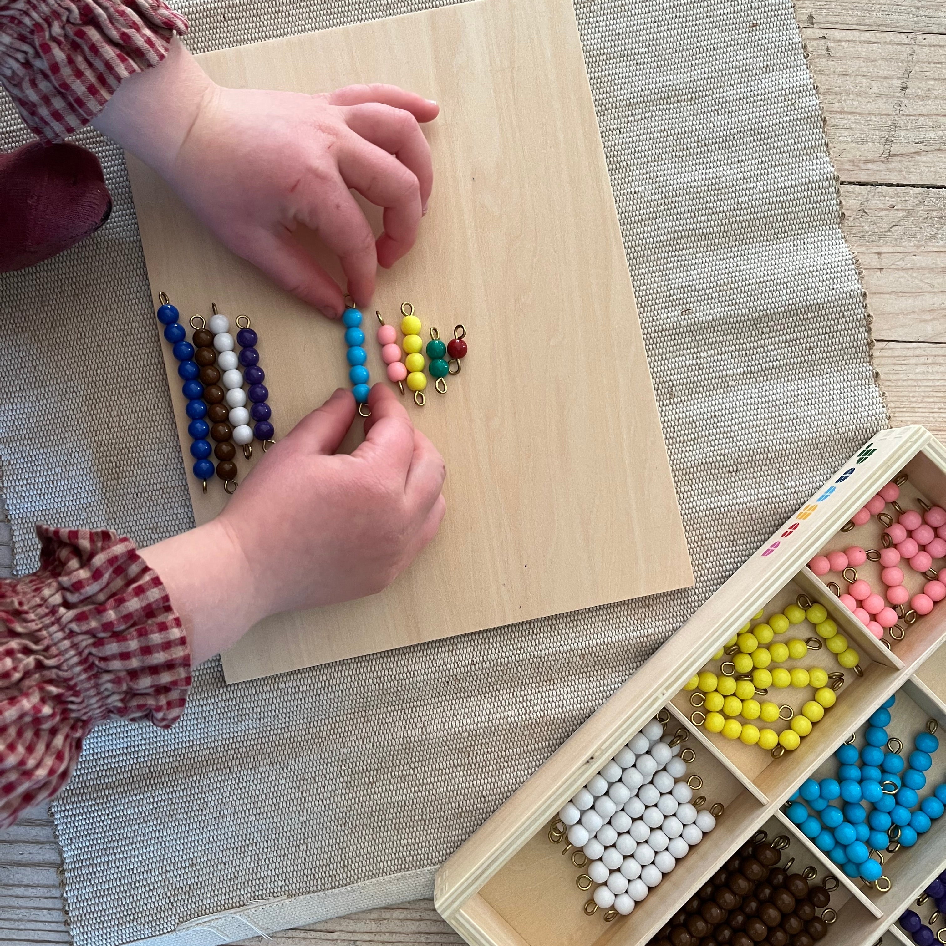 Et barn som sorterer Montessori Matteperler hjemme på et teppe.